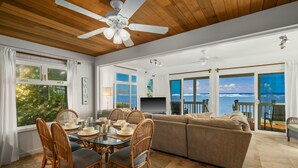 A spacious living area with a large window offering a view of the ocean, a dining table with chairs, and a sofa.