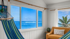 A room with a hammock, a striped chair, and a view of the ocean through large windows.
