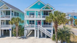 A two-story building with a balcony, a staircase, and palm trees. - 2nd Row 5 BR Beach House with a Private Pool! The Gathering Place  (Surfside Beach)