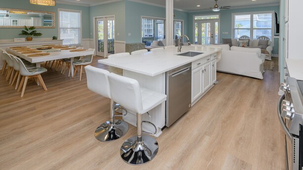 A spacious kitchen with a large island, white cabinetry, and a dining area with chairs and a table. - 2nd Row 5 BR Beach House with a Private Pool! The Gathering Place  (Surfside Beach)