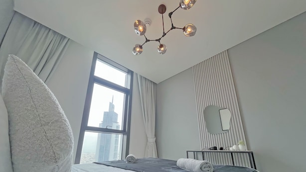 Un hotel moderno con una cama grande, una lámpara original, un ventanal con vista a la ciudad y un espejo en la pared.