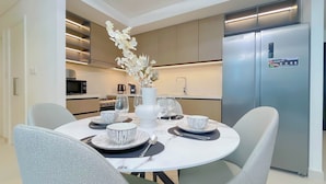 Una cocina moderna con refrigerador integrado, una mesa de comedor dispuesta con platos y tazones blancos, y un jarrón con flores blancas.