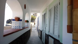 A corridor with a tiled floor, a bench, potted plants, and a door with shutters. - Little house by the sea (Acquacalda)