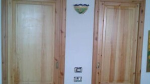 A room with two wooden doors, a small window, and a wall-mounted light switch. - Little house by the sea (Acquacalda)