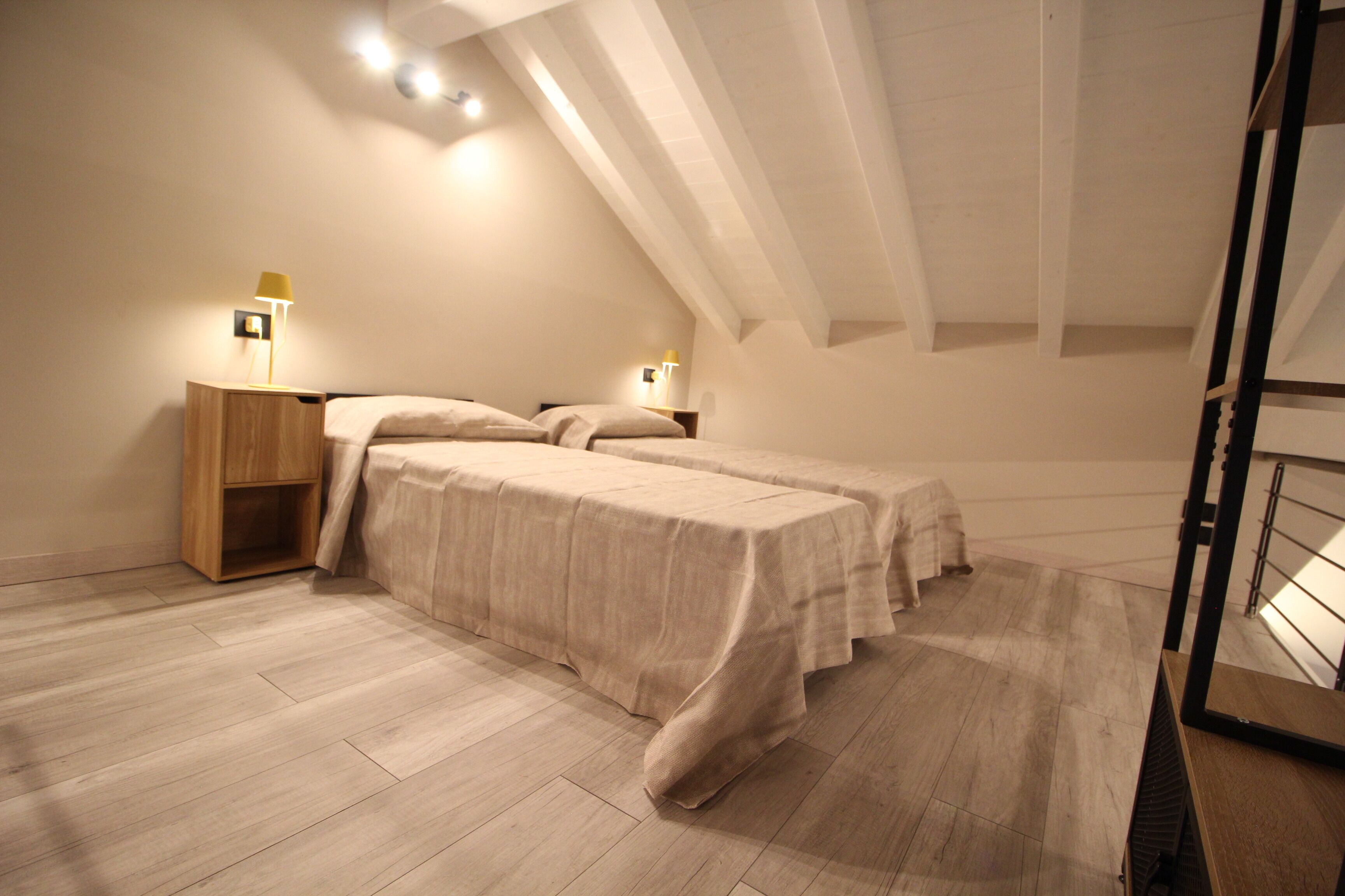 A bedroom with two beds, wooden nightstands, and wall-mounted lamps.