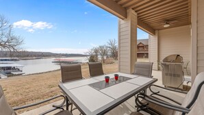 Une terrasse extérieure avec une table et des chaises, donnant sur un lac et une maison.