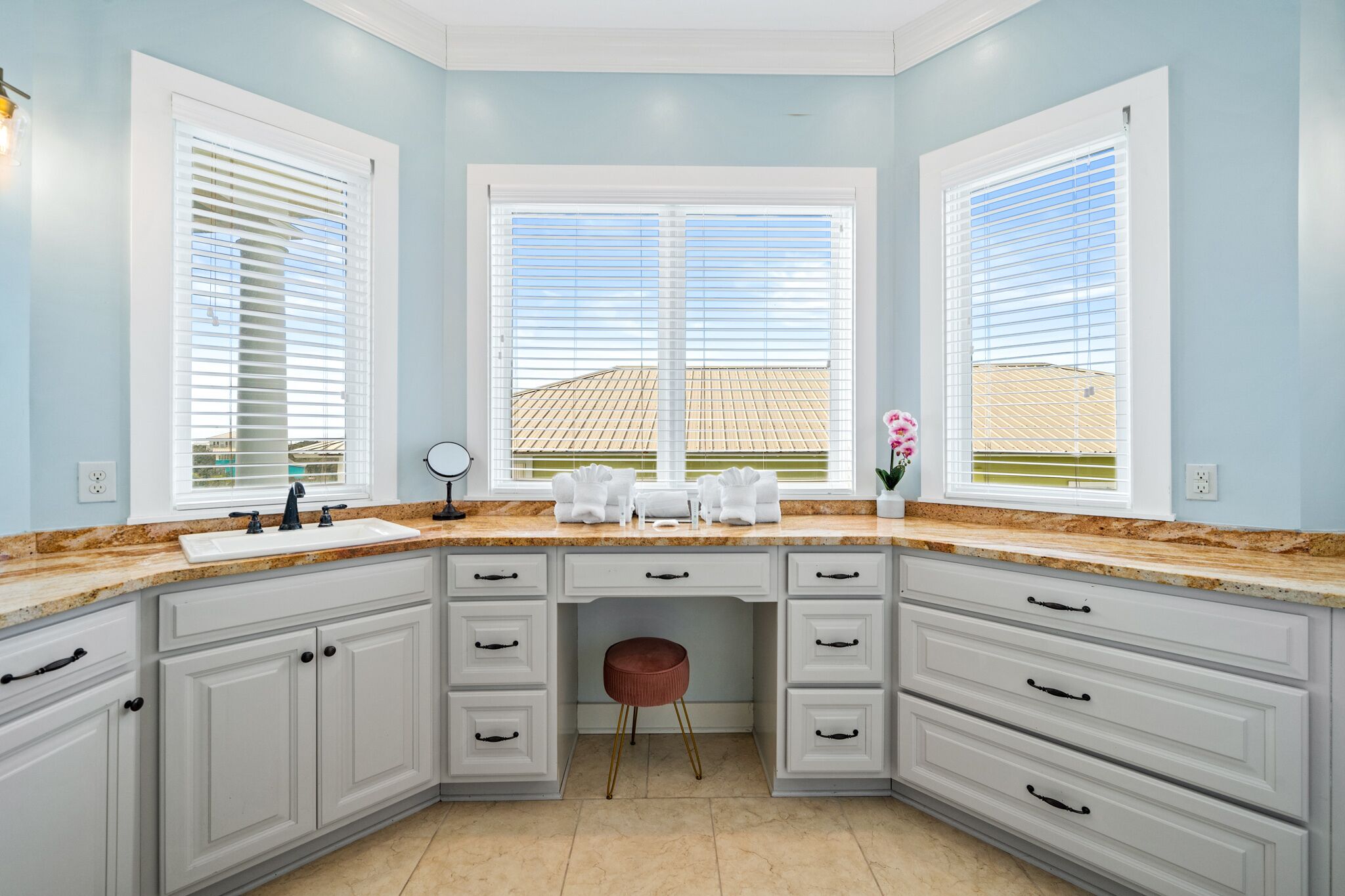 A kitchen with white cabinets, a marble countertop, and a view of a building through large windows.