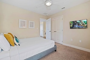 Une chambre à coucher avec un lit, un ventilateur de plafond, une porte et un téléviseur fixé au mur.