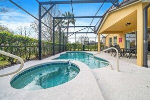 A swimming pool with a glass enclosure, surrounded by a patio area with chairs and tables.