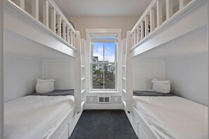Ein Zimmer mit zwei Etagenbetten, einem Fenster mit Blick auf eine Wohngegend und einem kleinen Heizgerät unter dem Fenster.