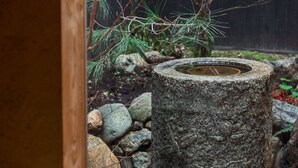 Ein Wasserbecken aus Stein, umgeben von Steinen und Kiefernzweigen.