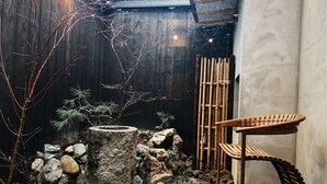 Ein rustikaler Sitzbereich im Freien mit einem Holzstuhl und einer Steinstruktur, umgeben von Steinen und Pflanzen.