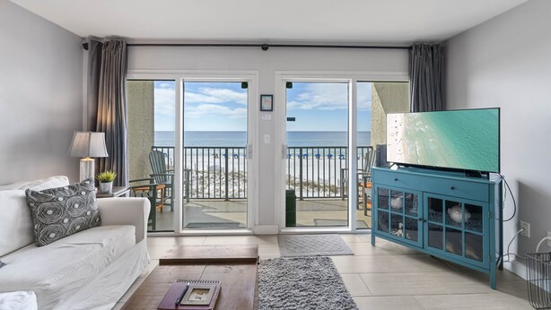 En stue med sofa, fjernsyn på et skab og udsigt til stranden gennem skydedøre.