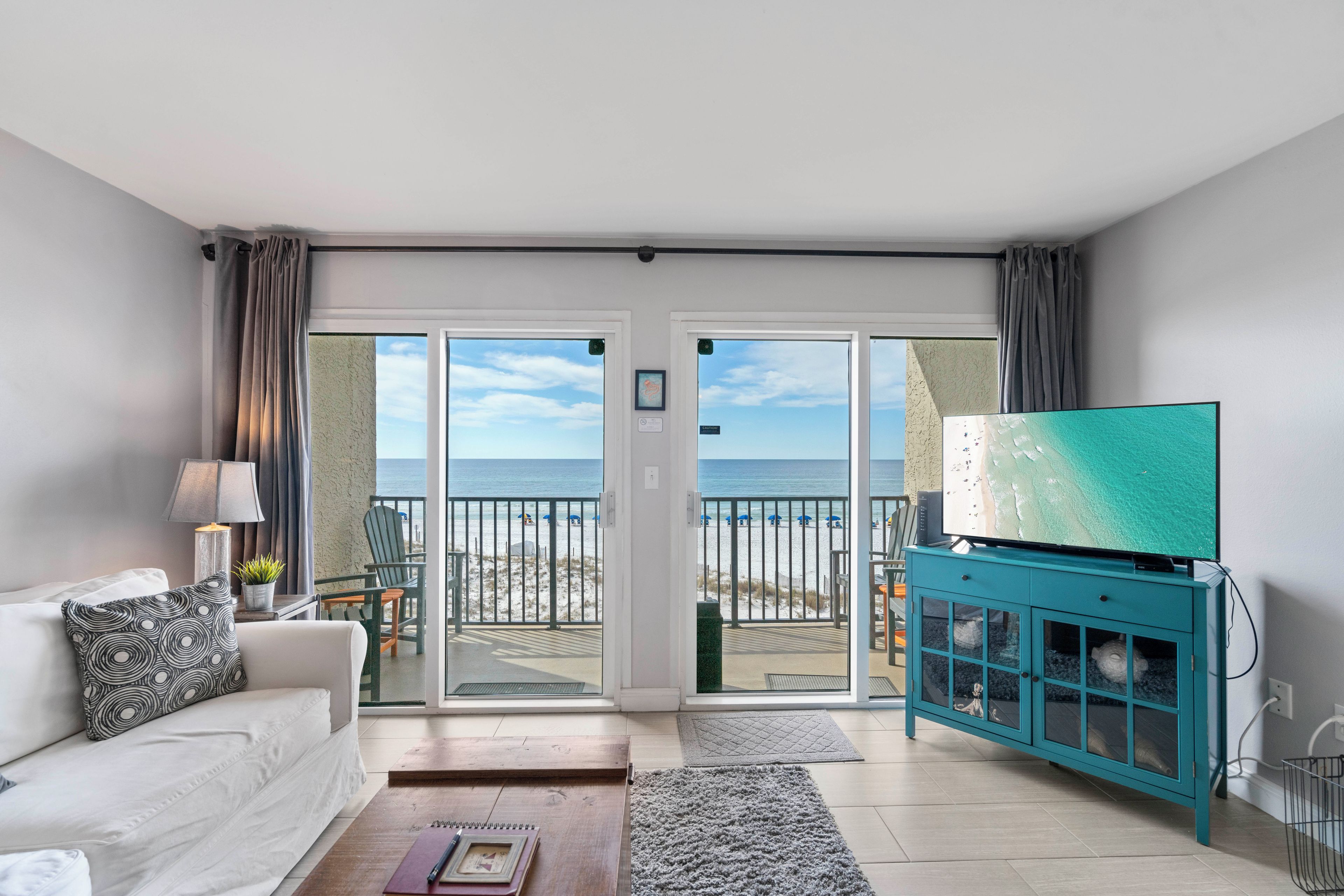 Uma sala de estar com um sofá, uma televisão sobre um móvel e vista para a praia através de portas de correr.