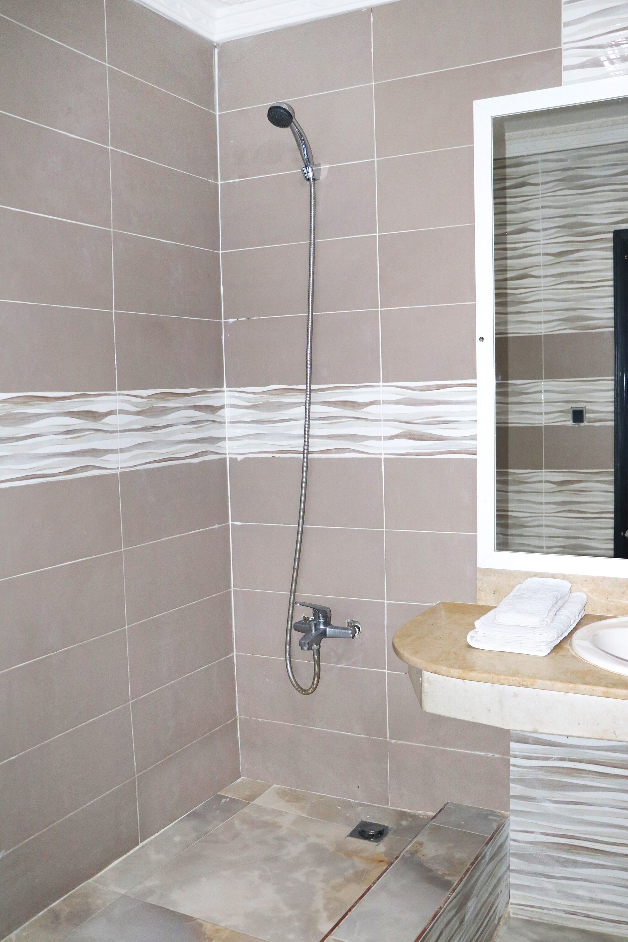Ducha con cabezal de ducha de mano, lavabo con espejo y paredes con azulejos.