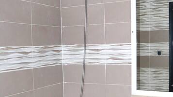 Ducha con cabezal de ducha de mano, lavabo con espejo y paredes con azulejos.