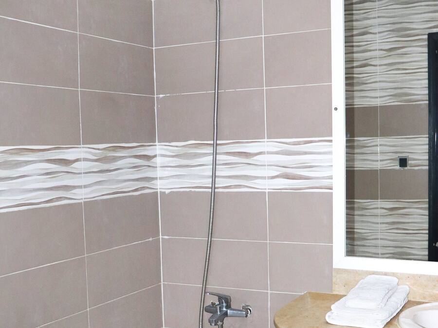 Ducha con cabezal de ducha de mano, lavabo con espejo y paredes con azulejos.