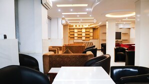 Un restaurante moderno con una larga mesa blanca, sillas de cuero negro y asientos tapizados en tonos rojo y marrón.