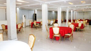 Un salón amplio con varias mesas redondas cubiertas con manteles rojos y sillas doradas.