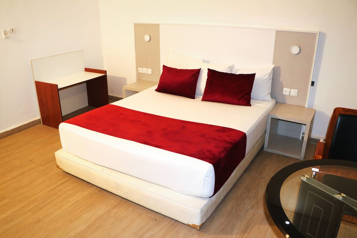 Una habitación de hotel ordenada con una cama grande, una mesita de noche, una silla y una pequeña mesa.
