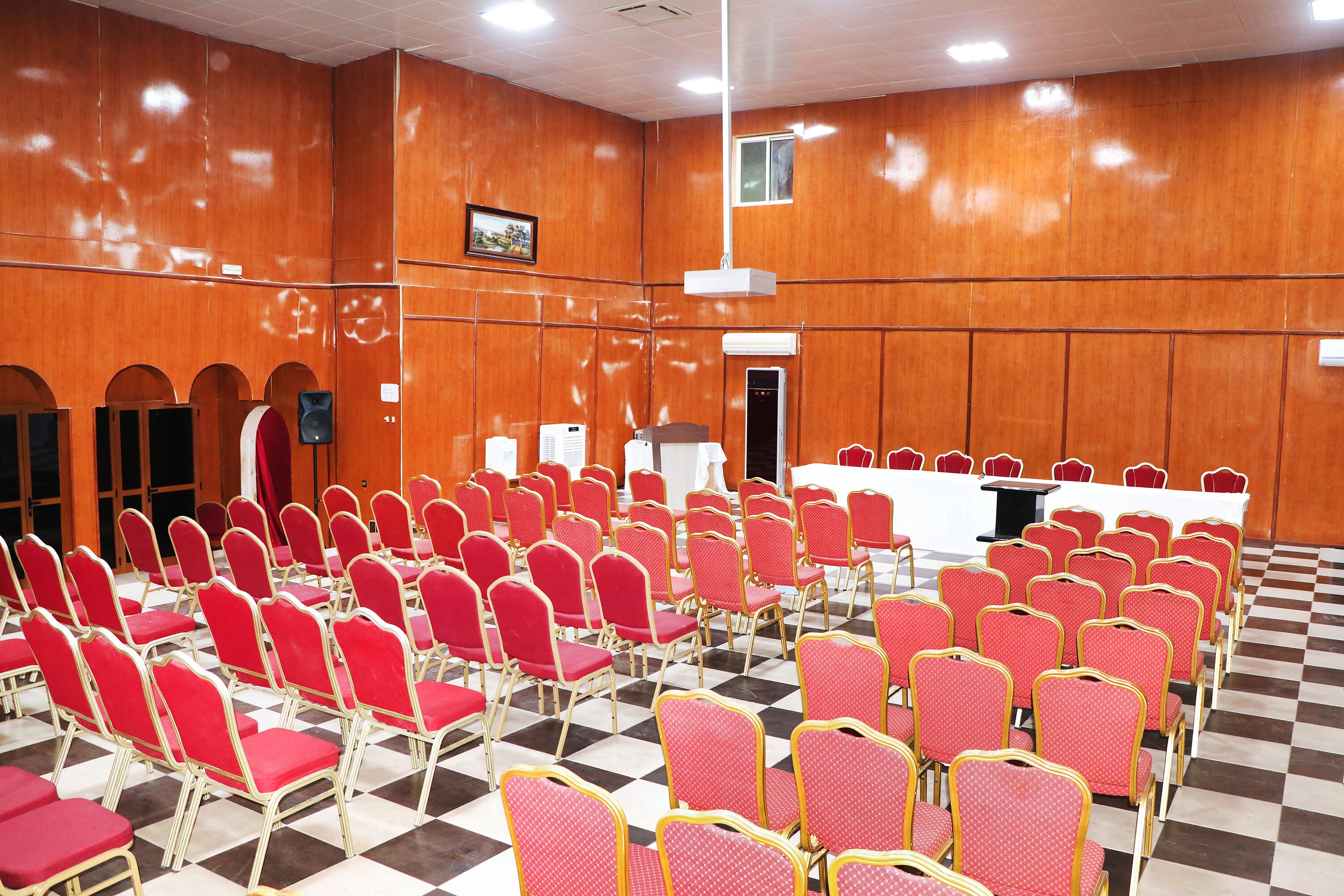 Un salón de conferencias con hileras de sillas rojas, una mesa blanca y un atril.