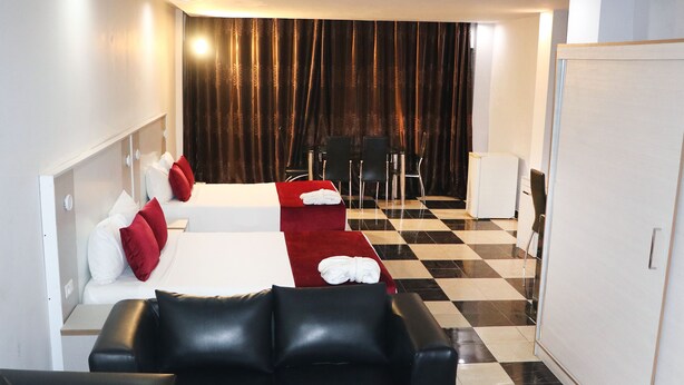 Habitación de hotel con dos camas, un sofá de cuero negro, una mesa de comedor con sillas y suelo a cuadros.
