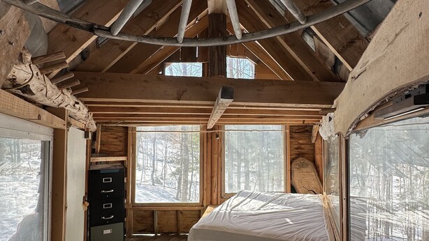 A cabin with a wooden interior, a bed, a dresser, and large windows. - Streeter Mountain Farm (Rumney)