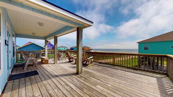 A wooden deck with outdoor seating, a covered area, and a view of the ocean.