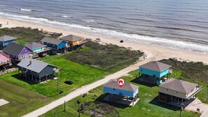 An aerial view of a coastal residential area with houses on stilts, a beach, and a clear sky.