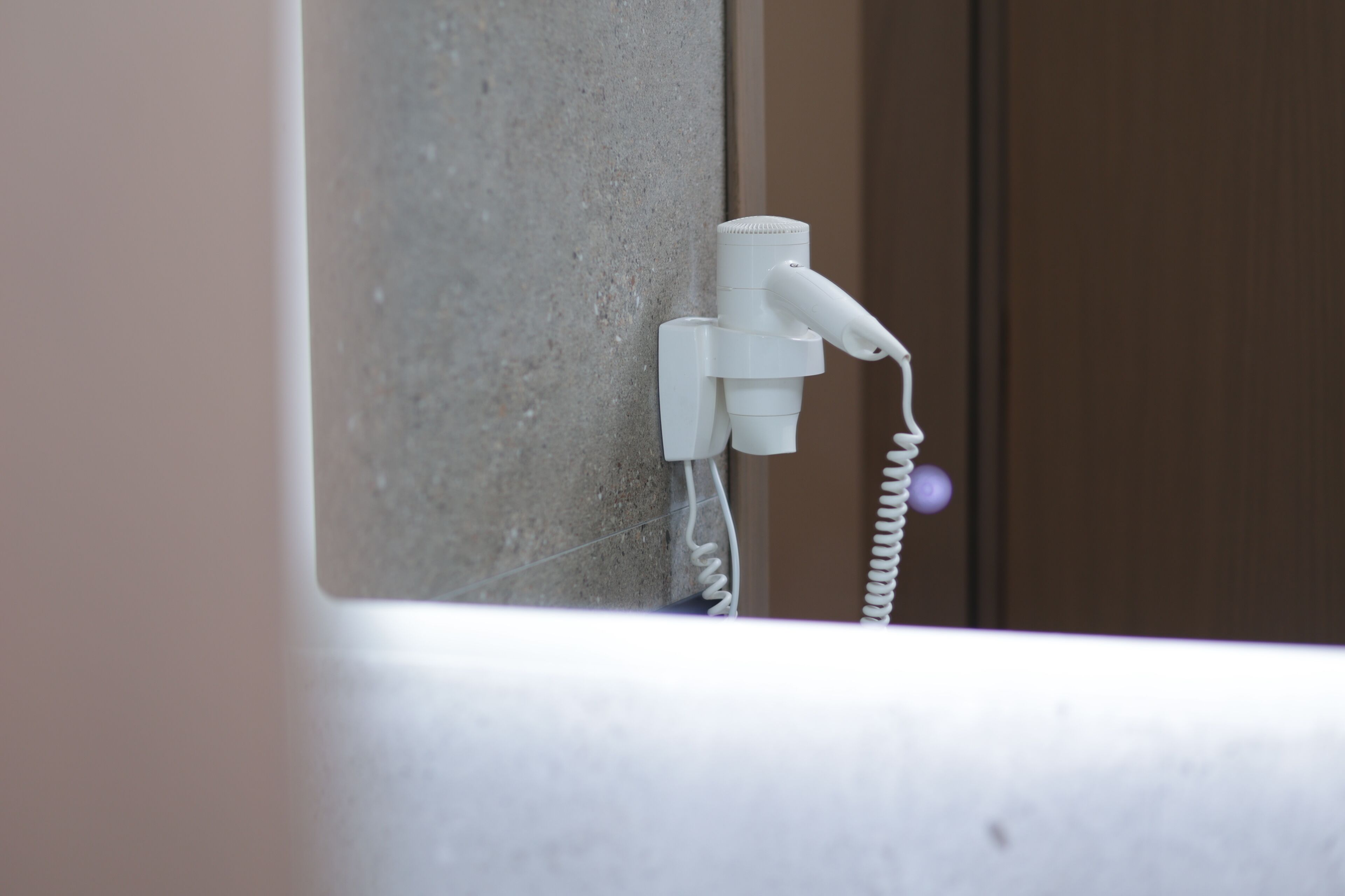 A white hairdryer mounted on a wall near a door.