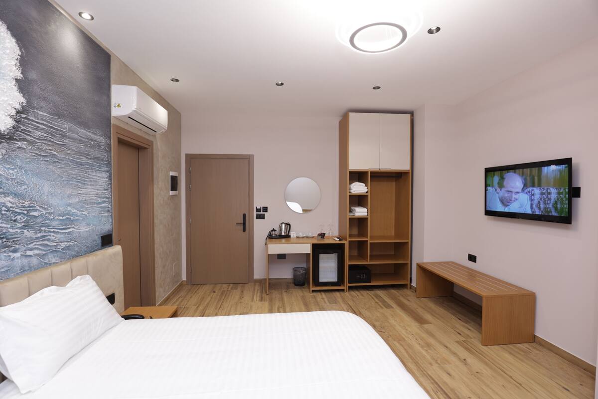 A modern hotel room with a large bed, a desk, a TV, and a wardrobe.