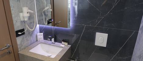A modern bathroom with a marble vanity, a white sink, a toilet, and a trash bin.