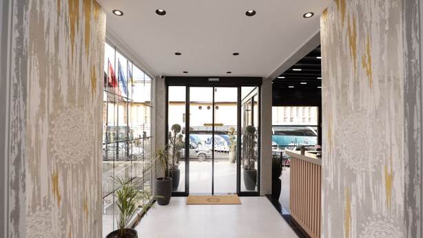 A hotel entrance with a glass door, potted plants, and a view of parked cars outside. - Residence Inn Hotel (Tirana)