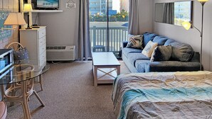 Ein Hotelzimmer mit Balkon, einer Couch, einem Schreibtisch, einem Sessel und einem Fernseher.