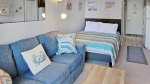Ein Zimmer mit einem blauen Sofa, einem Bett mit gestreifter Bettwäsche, einem Holztisch und einer Tür mit einem Schild.