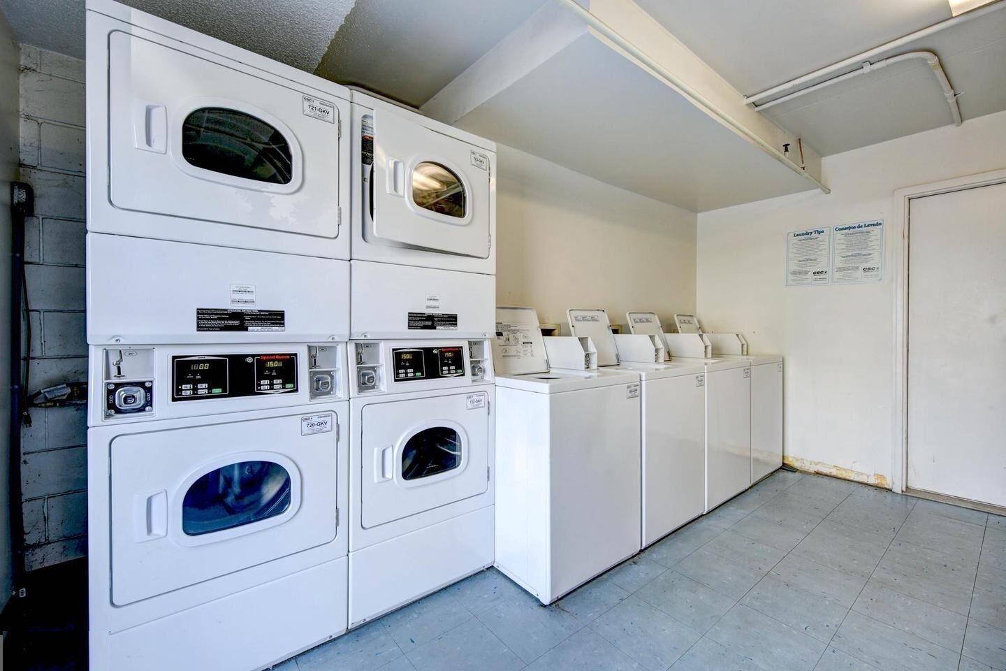 A laundry facility with stacked washers and dryers, control panels, and instructional signs.
