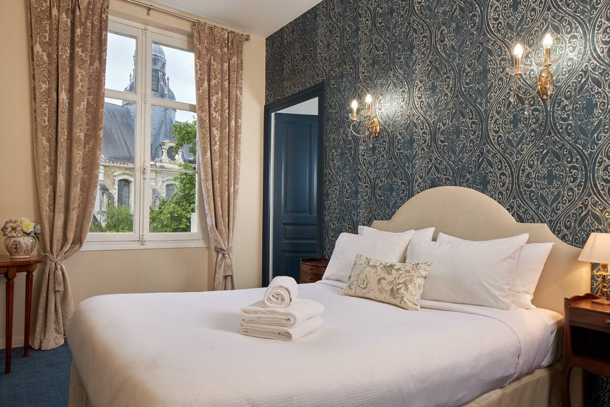 A hotel room with a large bed, a view of a historic building, and a patterned wallpaper.