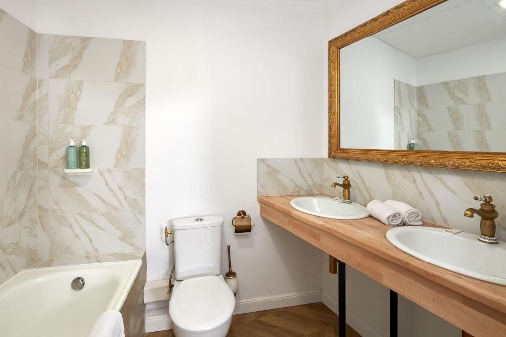 Une salle de bain avec un mur en marbre, une baignoire, des toilettes, un lavabo et un miroir.