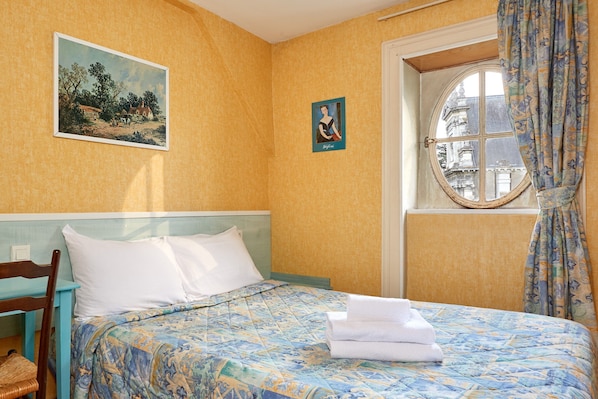 Quarto de hotel com uma cama, janela com cortinas, um quadro na parede e uma fotografia emoldurada.