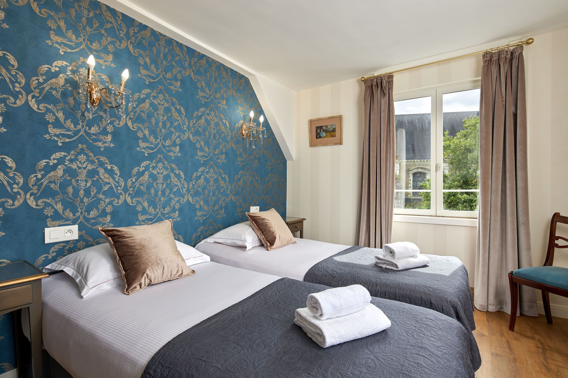 A hotel room with two beds, a window with curtains, a chair, and a wall with a decorative pattern.