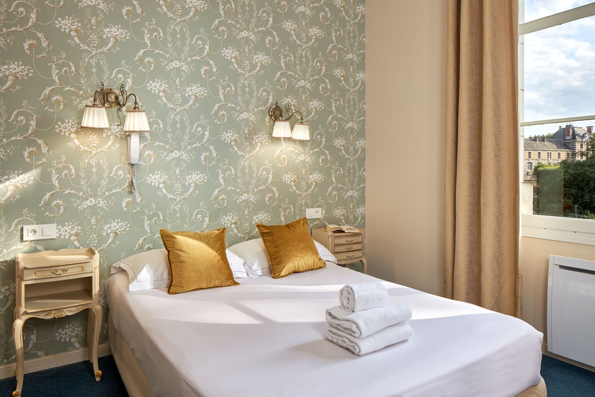 Une chambre d’hôtel avec un lit, deux lampes de chevet, une table de chevet et une fenêtre avec des rideaux.