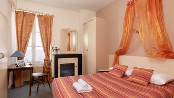 Una habitación de hotel con una cama, un escritorio con lámpara, una silla y una chimenea.