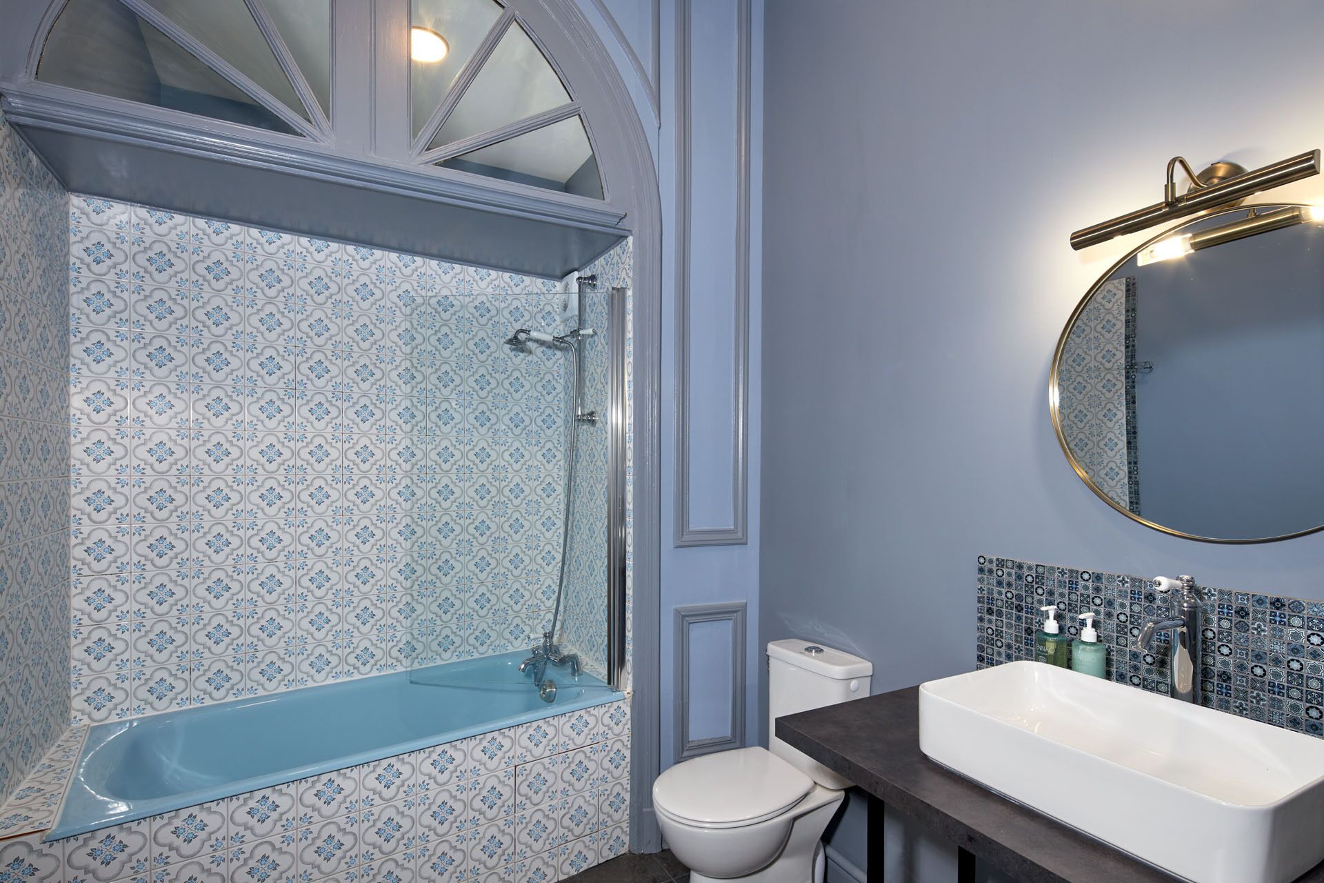 Une salle de bain avec une douche aux carreaux bleus, des toilettes blanches et un lavabo surmonté d’un miroir.