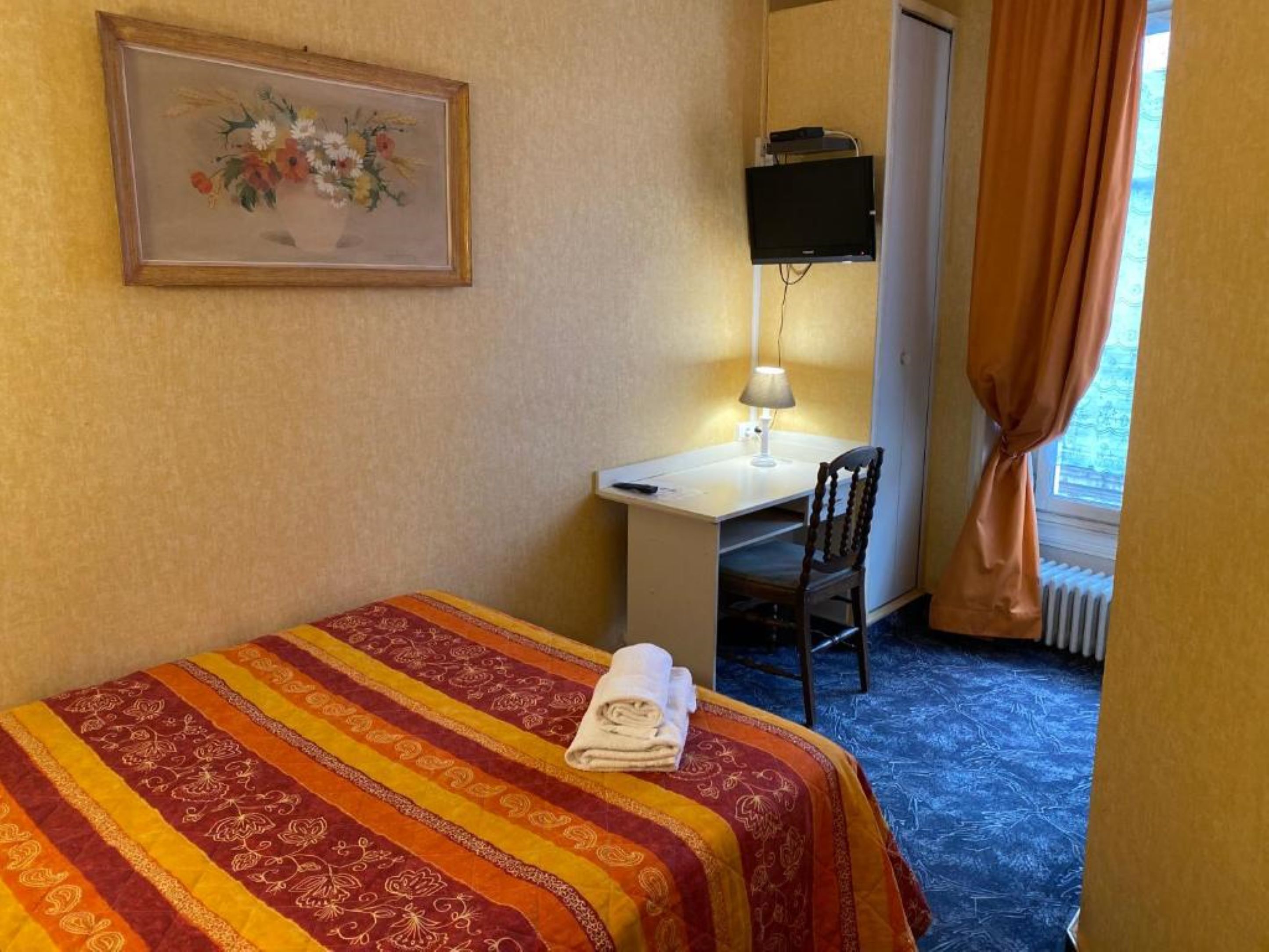 A hotel room with a bed, a desk, a chair, a TV, and a window with curtains.