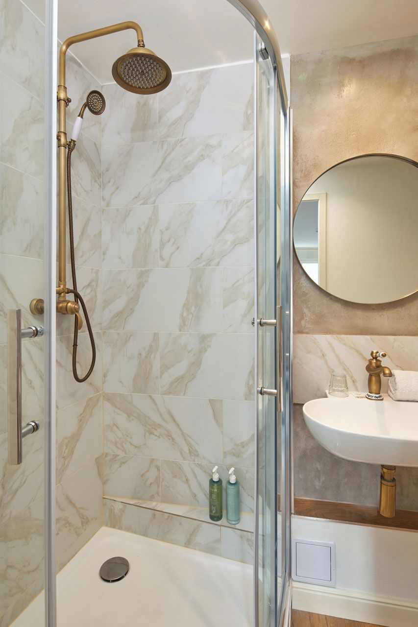 A shower with a handheld showerhead and a rain shower head, a glass door, and a marble-tiled wall.