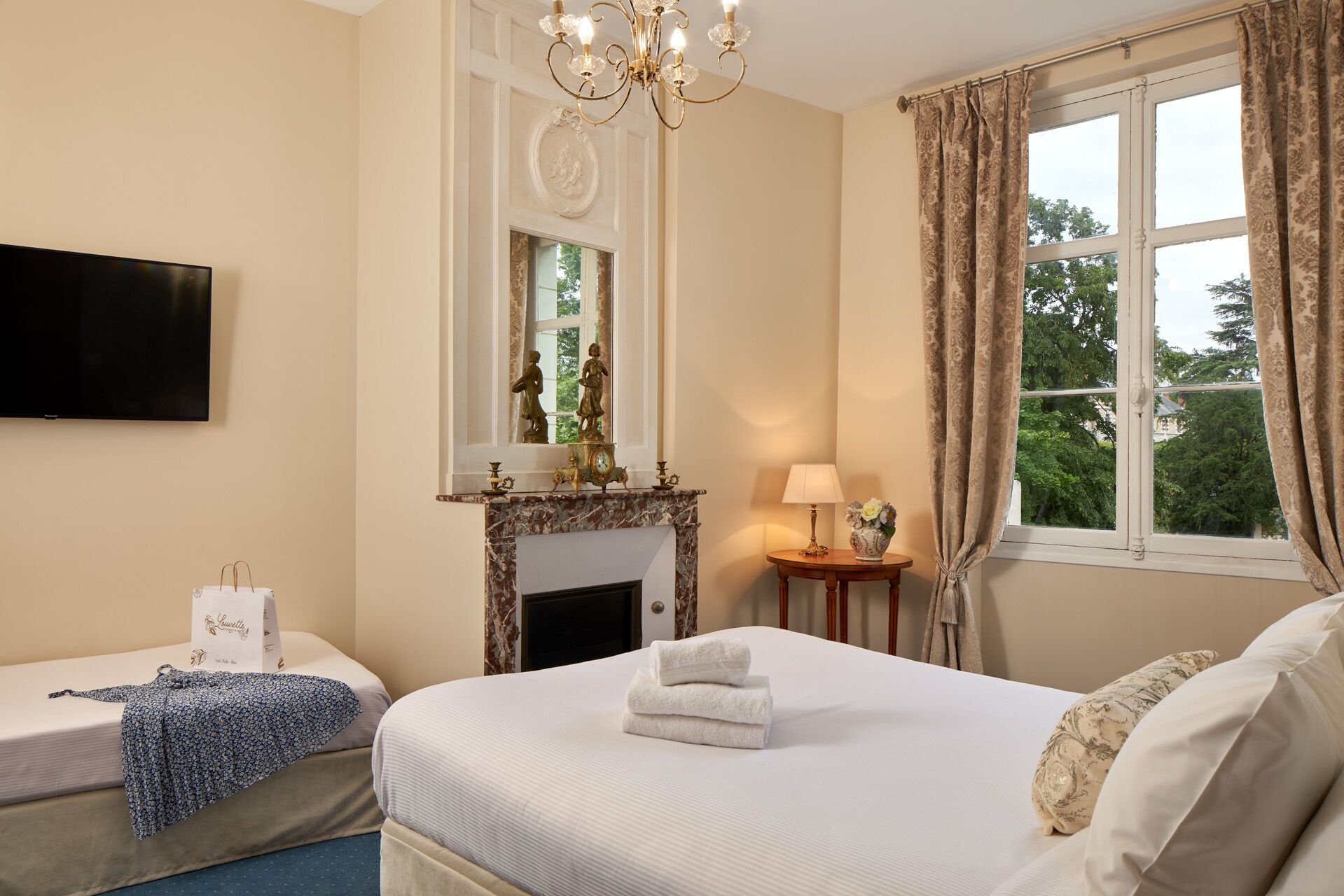 Une chambre d’hôtel avec un lit, une télévision, une cheminée et une fenêtre avec des rideaux.