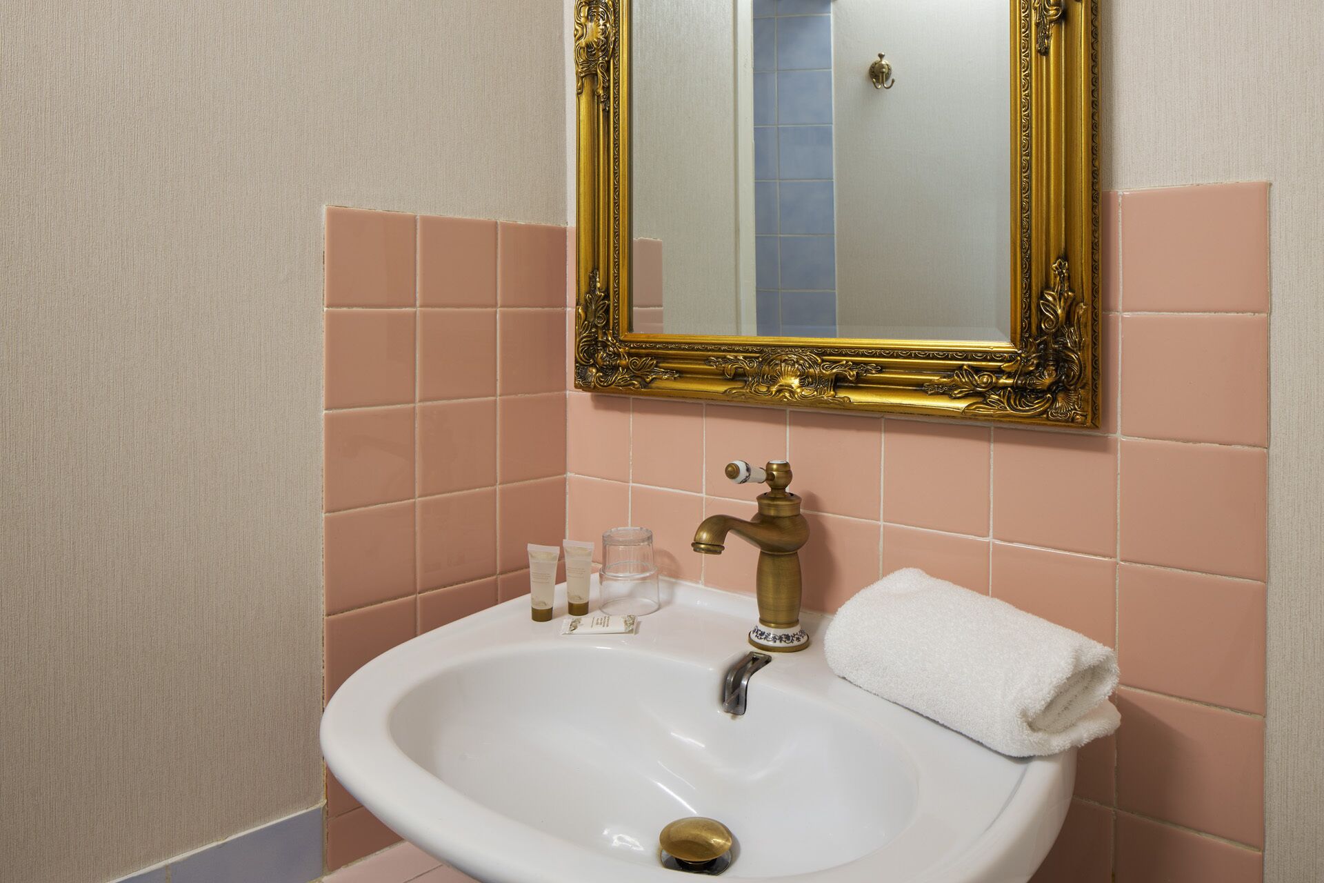 A bathroom with a white sink, gold faucets, and a gold-framed mirror.
