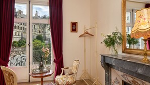 Una habitación con un ventanal grande, una chimenea, un espejo y una silla con estampado floral.