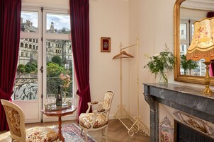 Une pièce dotée d’une grande fenêtre, d’une cheminée, d’un miroir et d’un fauteuil à motifs floraux.