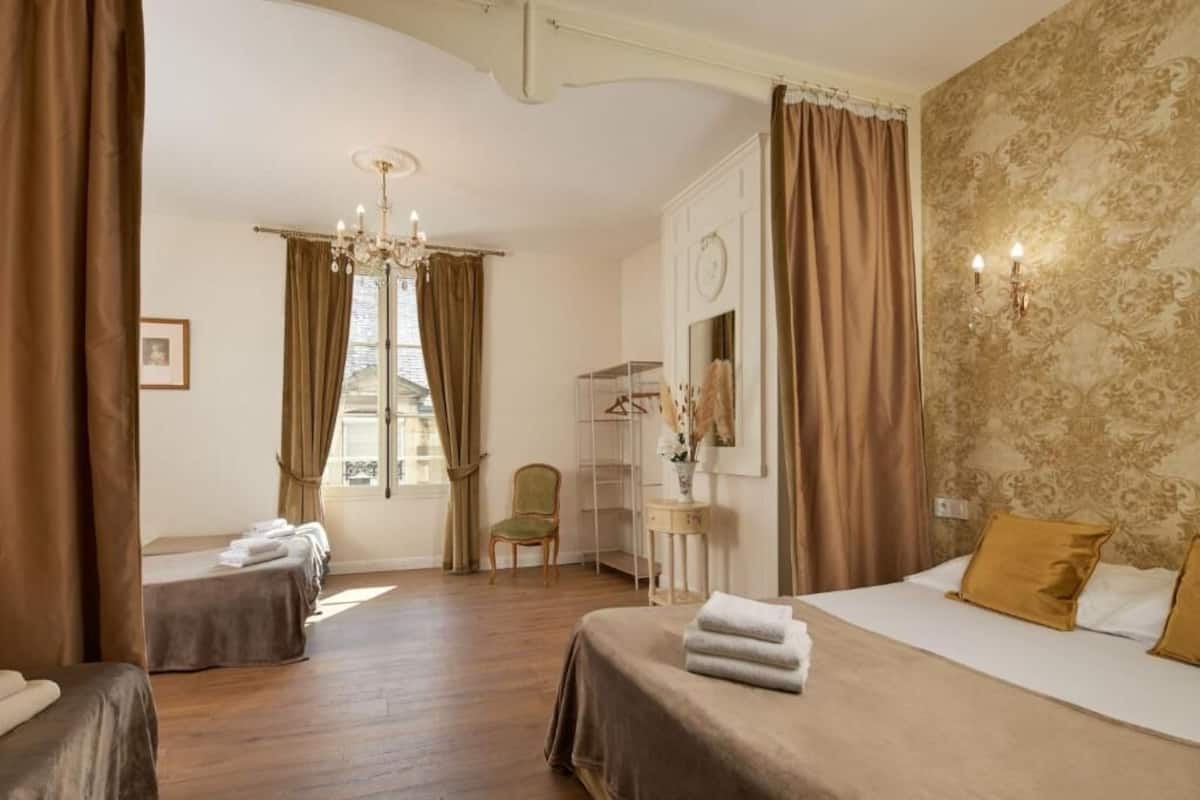 A hotel room with a bed, a chair, a small table with a vase, and a window with curtains.